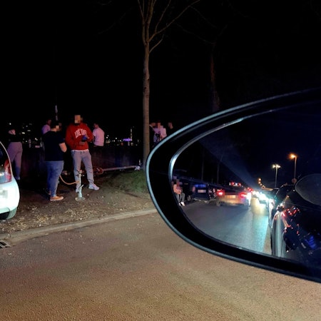 Junge Männer stehen um geparkte Autos auf der Alfred-Schütte-Allee herum und rauchen Shisha.