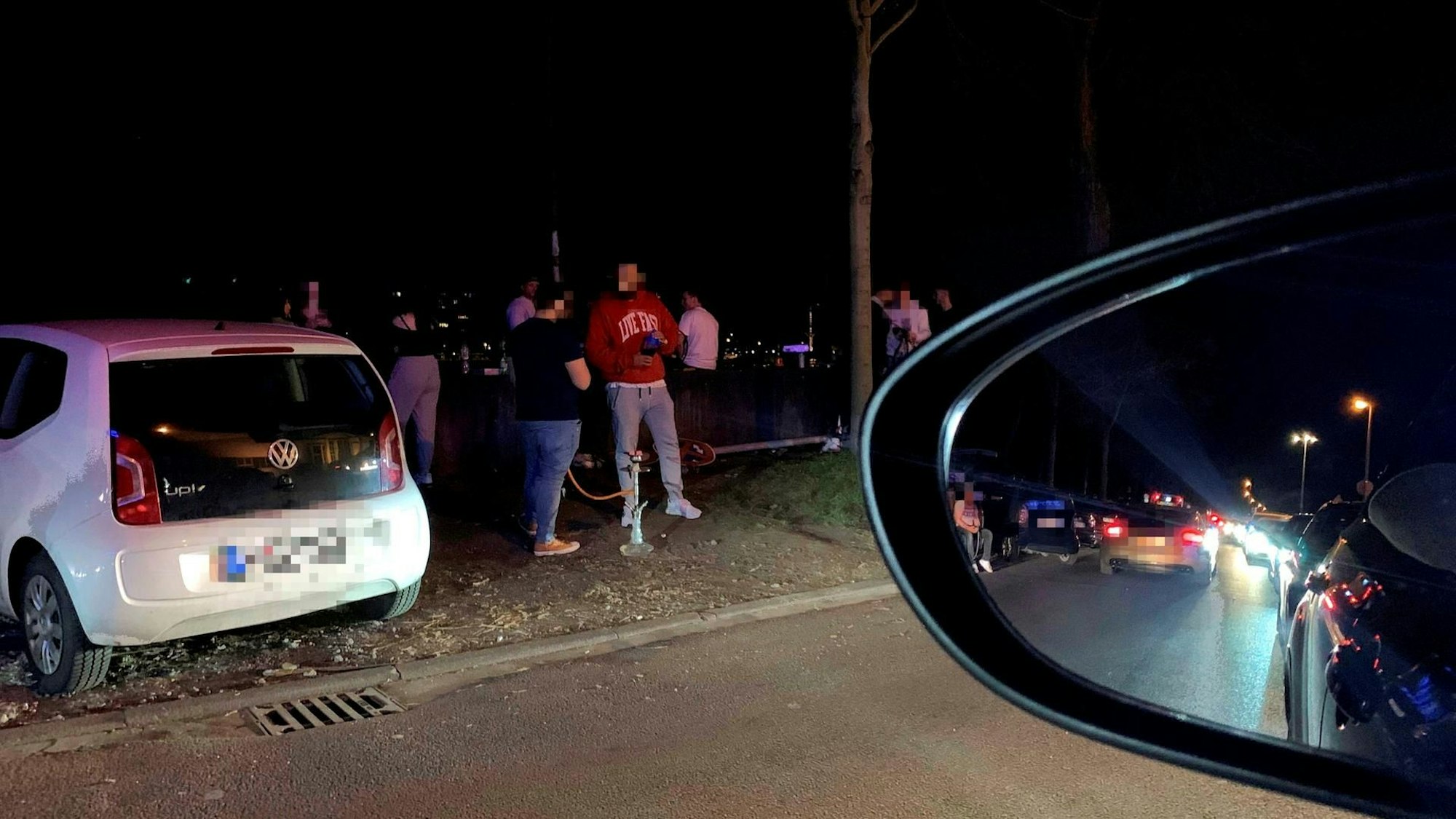 Junge Männer stehen um geparkte Autos auf der Alfred-Schütte-Allee herum und rauchen Shisha.