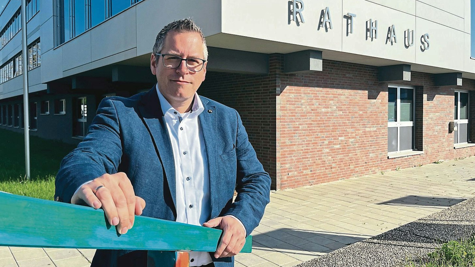Sascha Solbach (SPD), Bürgermeister von Bedburg, steht hinter einem Treppengeländer vor seinem Rathaus. Solbach hat graues kurzes Haar und trägt eine Brille.