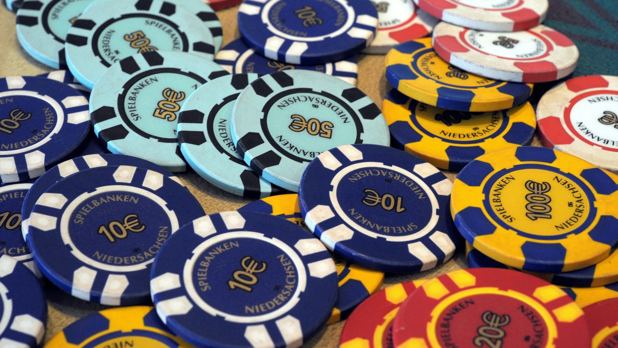 Glücksspielchips liegen auf einem Tisch. Sie haben unteschiedliche Farben.
