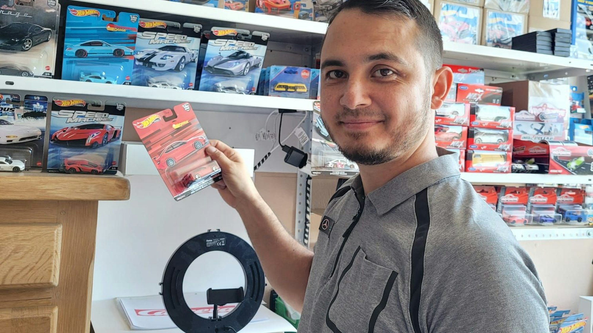Ozan Demir steht vor einem Regal mit zahlreichen Fahrzeugen. Er hält einen roten Sportwagen in der Hand.
