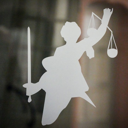 Die Figur der Justitia mit Richtschwert und Waage ist auf dem Glasfenster einer Tür im Gerichtsgebäude zu sehen.