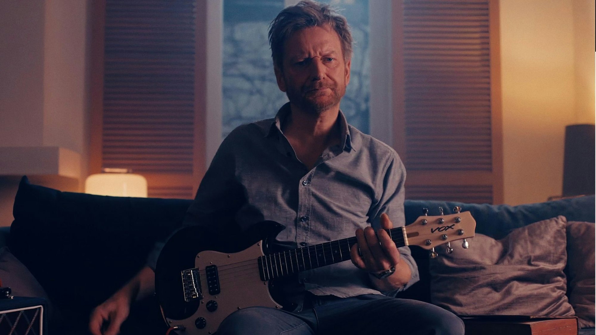 Ein Mann sitzt mit einer Gitarre auf einer Couch.