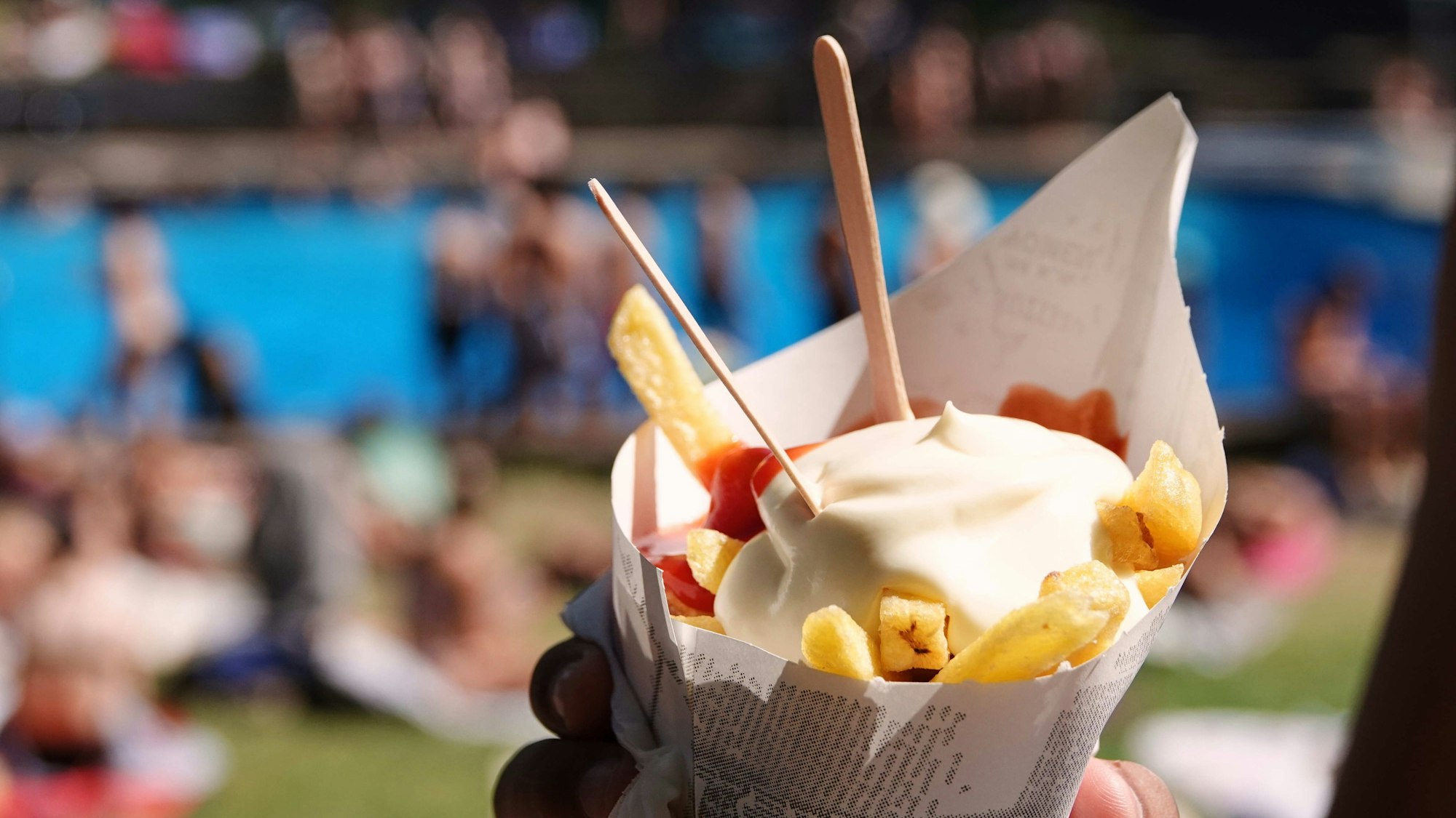 Ein Badegast hält eine Portion Pommes Frites mit Ketchup und Mayonnaise im Freibad in den Händen