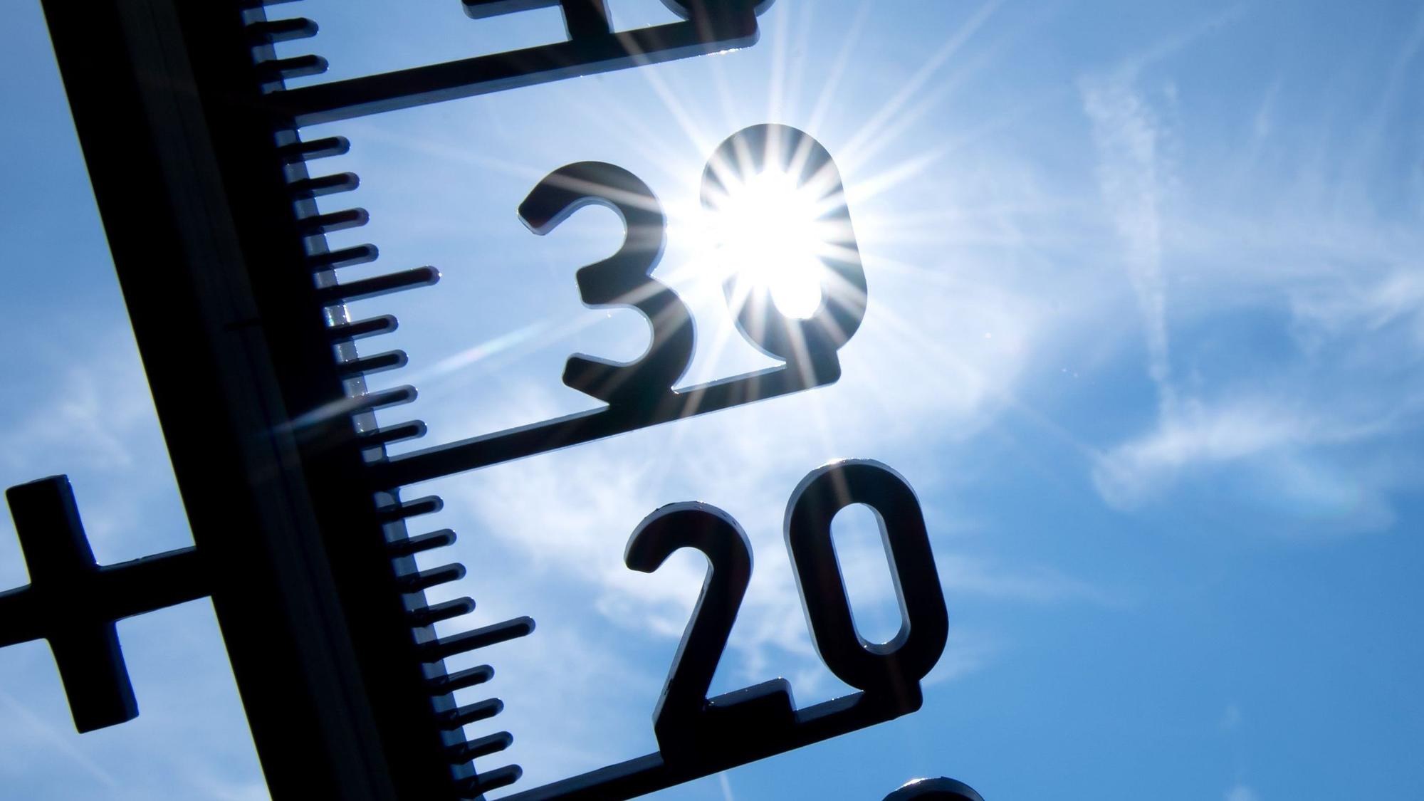 Blick auf ein Thermometer, im Hintergrund scheint die Sonne.