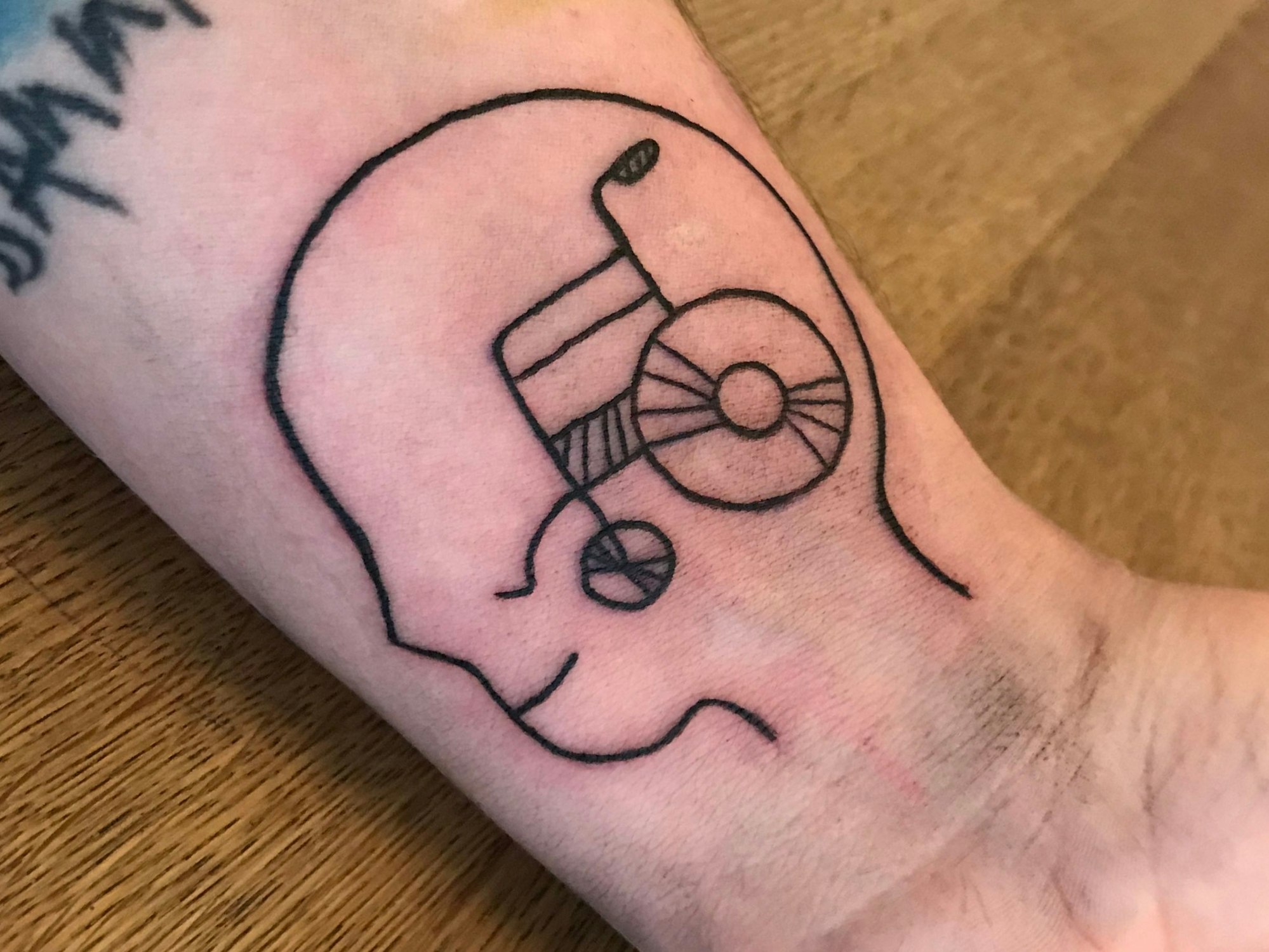 Eine Tätowierung zeigt den Umriss eines Kopfes und darin einen Rollstuhl.