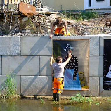 Zwei Bauhofmitarbeiter und der Kurator Jürgen A. Roder installieren die Werke der diesjährigen Ausstellung.