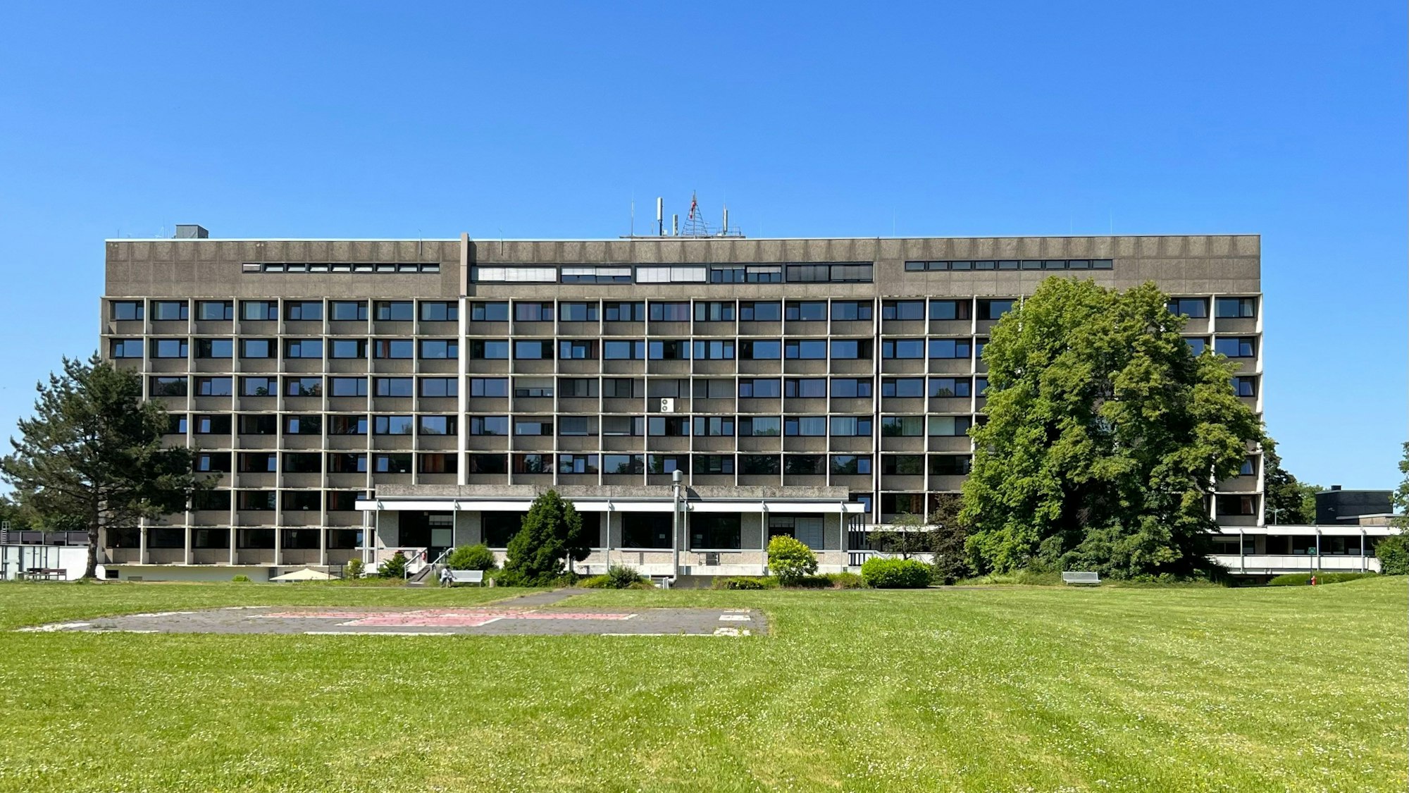 Das Krankenhaus Porz ist von hinten zu sehen. Ein enormer rechteckiger Kasten mit Fenstern, davor eine grüne Rasenfläche.