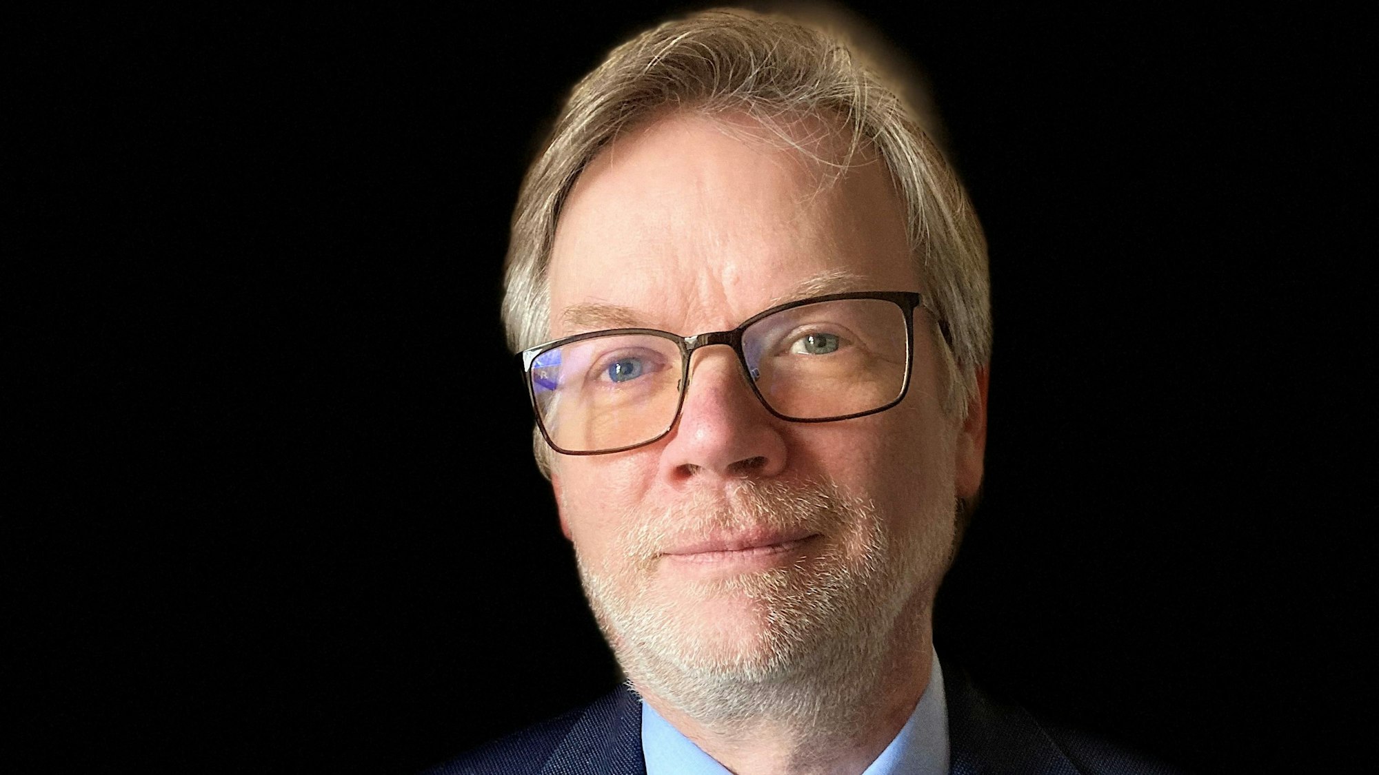 Guido Halbig guckt für ein Porträtfoto in die Kamera. Er trägt einen Anzug, hat blonde Haare und eine Brille.