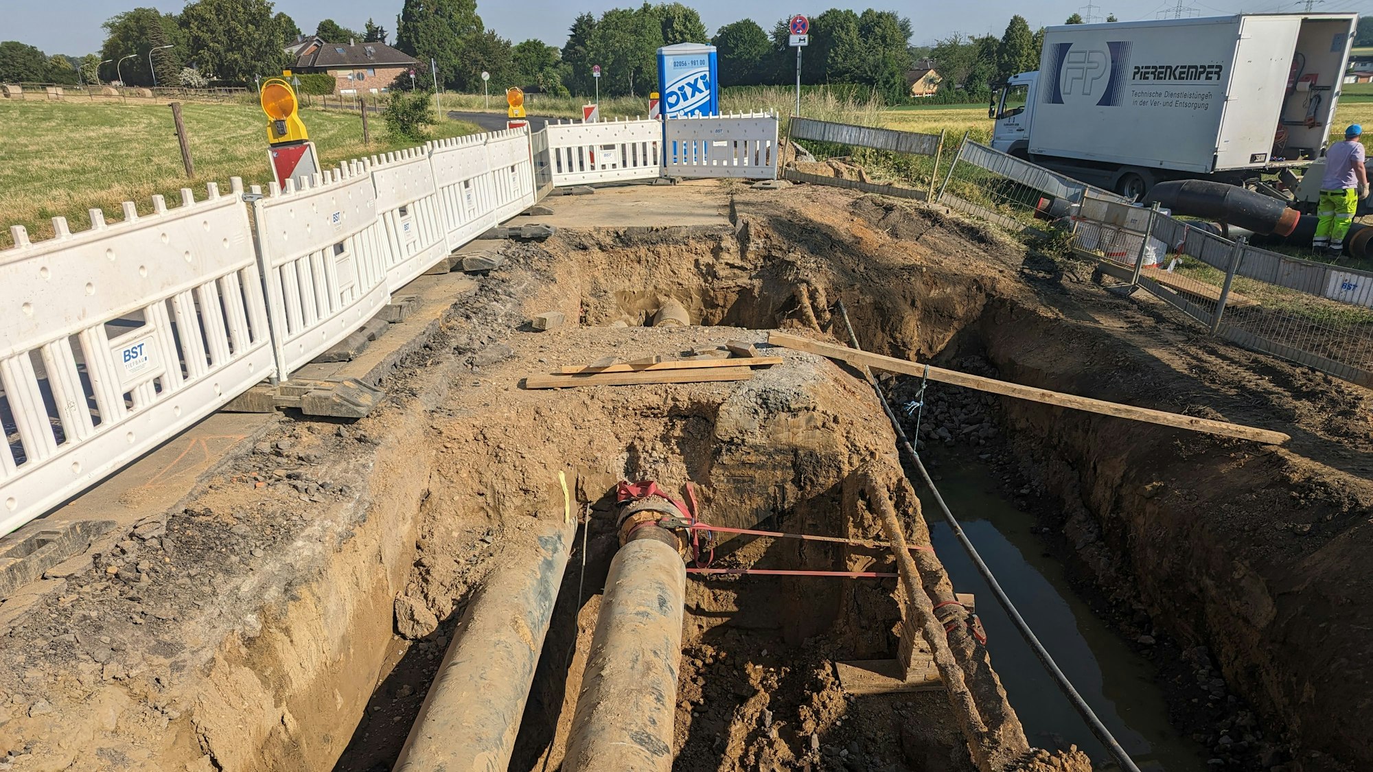 Zwei dicke Fernwärmeleitungen in einer ausgehobenen Baugrube.