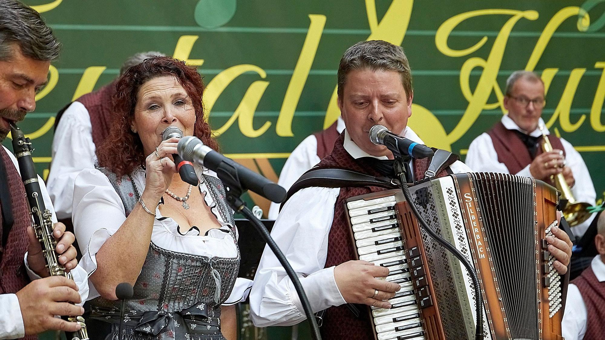 Das Bild zeigt eine Sängerin, die von mehreren Musikern mit verschiedenen Instrumenten begleitet wird.