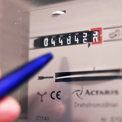 Ein Mensch tippt mit einem Kugelschreiber auf einen Stromzähler.