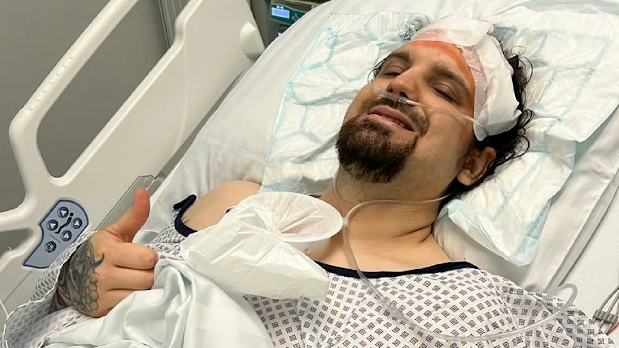 Der Kölner Johannes Olk liegt nach einer Gehirntumor-OP im Krankenbett, er ist mit Schläuchen verkabelt und streckt den Daumen aus.