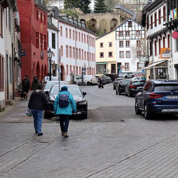 Blick in die Marktstraße in Bad Münstereifel, auf der ein Auto und Fußgänger unterwegs sind. Am Straßenrand parken weitere Autos.