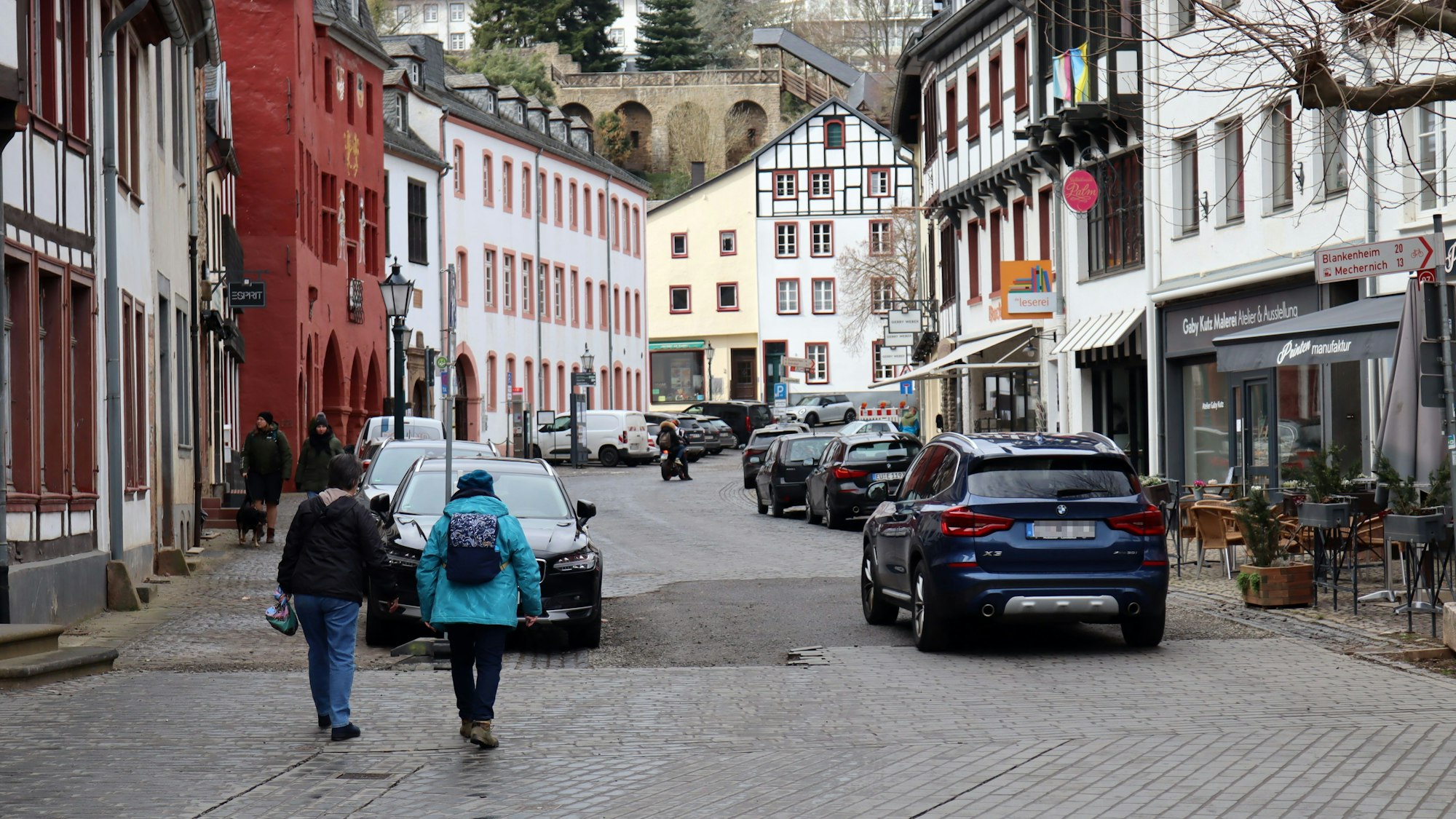 Blick in die Marktstraße in Bad Münstereifel, auf der ein Auto und Fußgänger unterwegs sind. Am Straßenrand parken weitere Autos.
