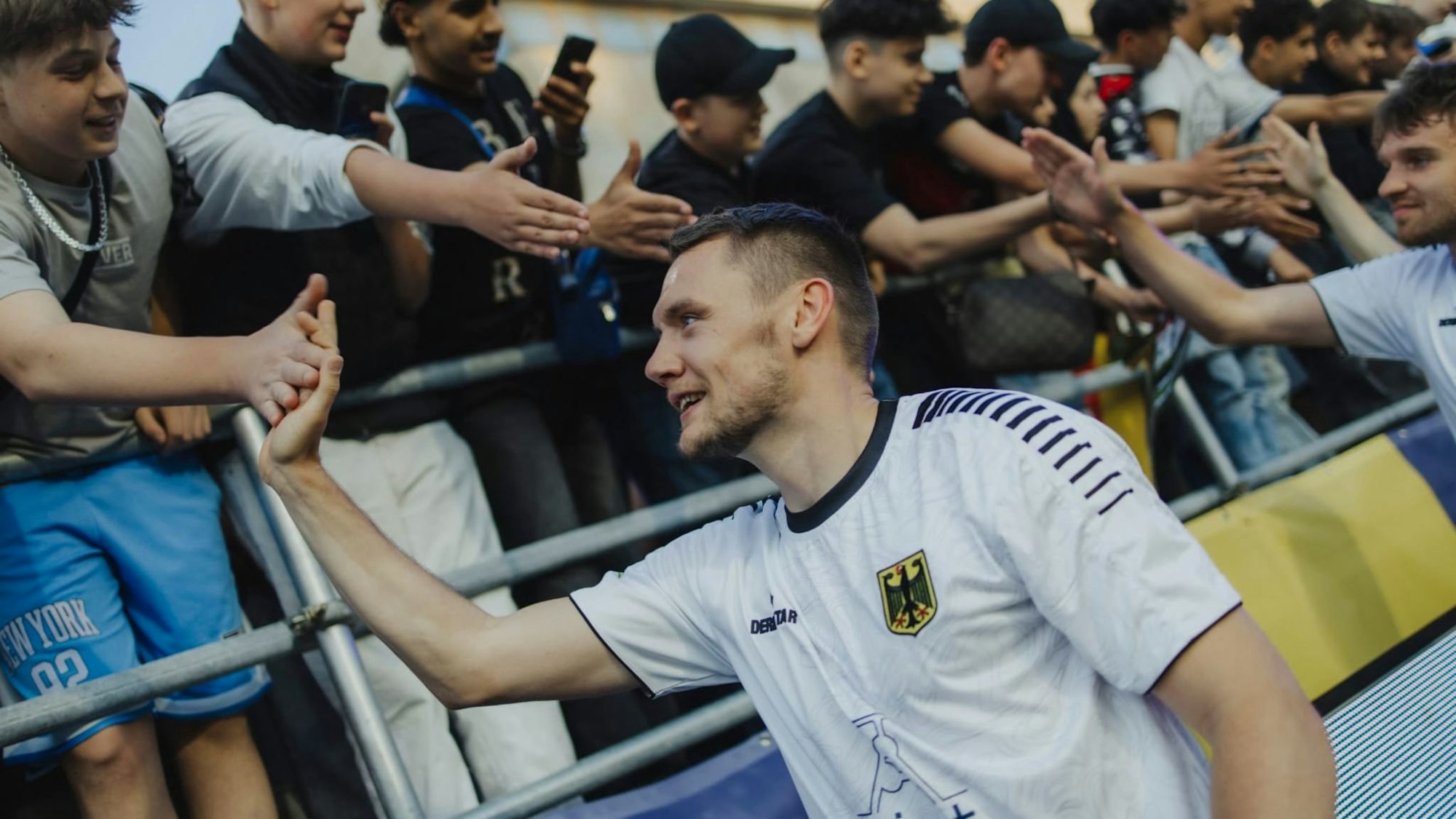 Ein Mann im deutschen Nationaltrikot schlägt mit Fans an einer Tribüne ab.
