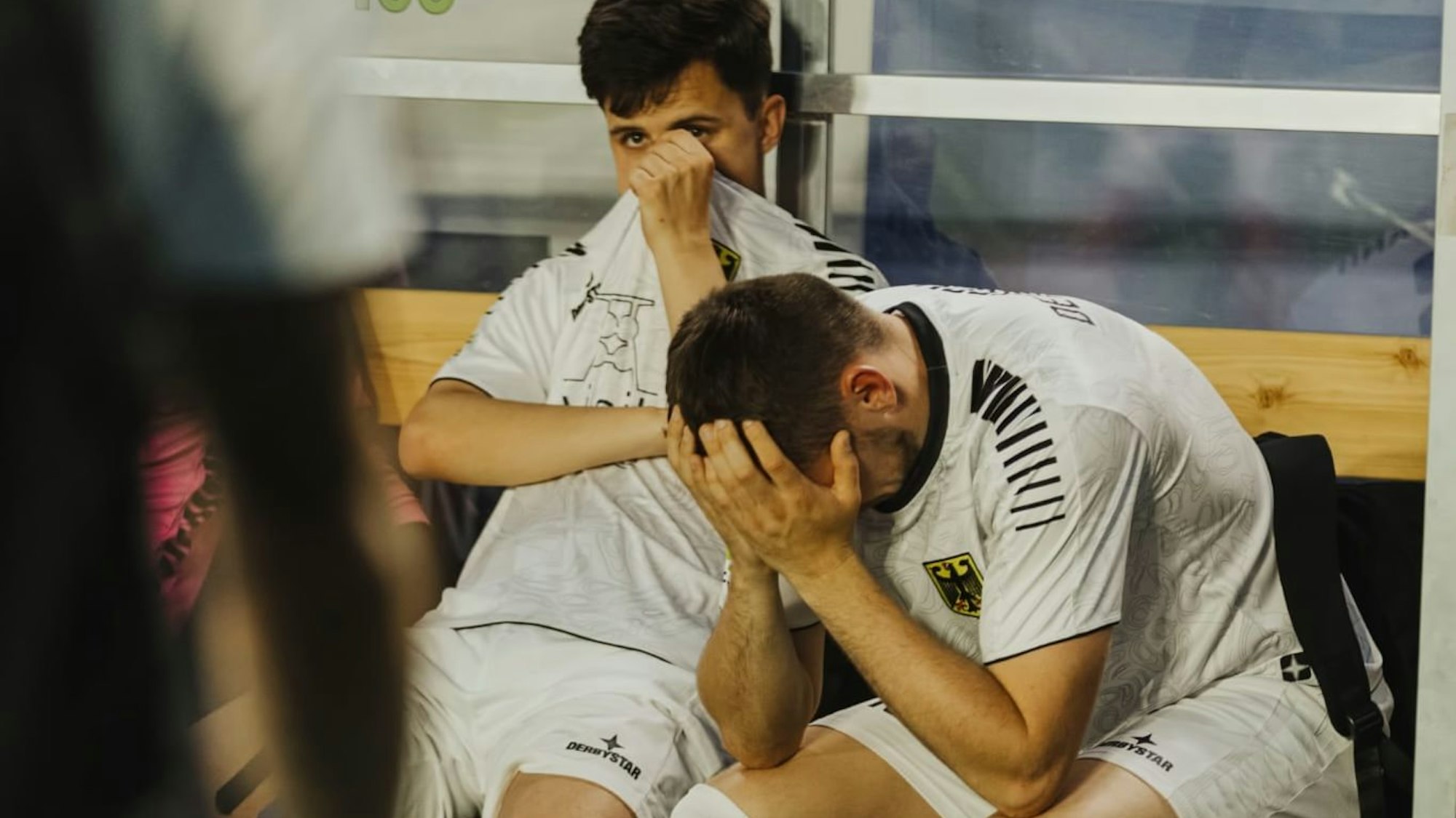 Ein Fußballer sitzt auf der Bank am Spielfeldrand und vergräbt den Kopf in den Händen.