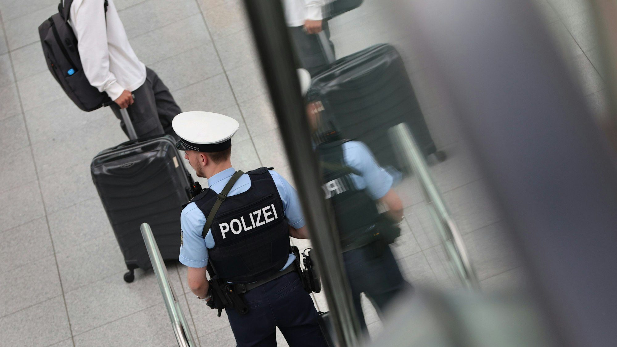 Ein Bundespolizist steht beim Besuch von Bundesinnenministerin Faeser auf dem Flughafen München an einer Rolltreppe vor Reisenden.
