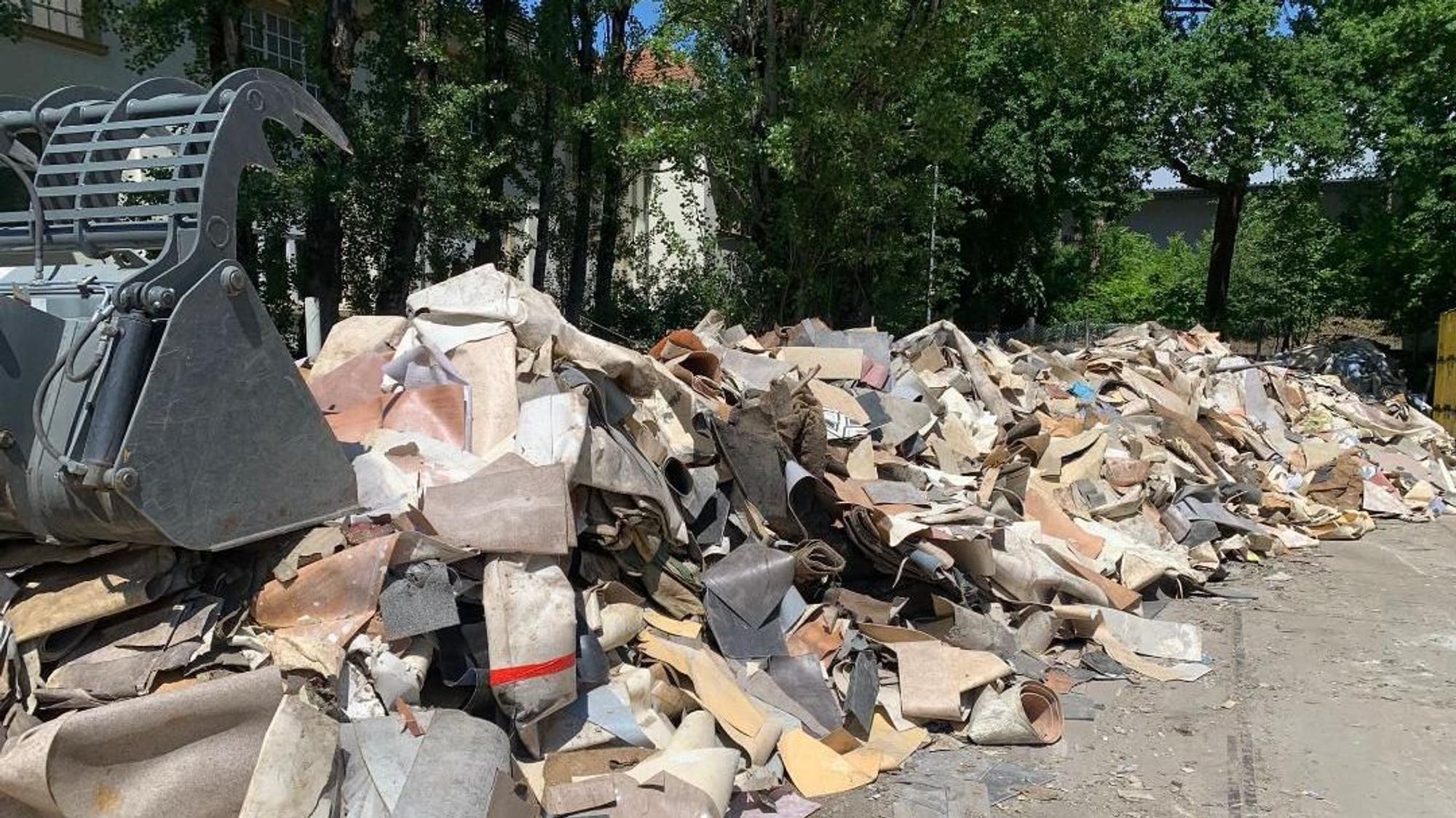 PVC-Recycling bei der Troisdorfer Firma „Gerflor Mipolam“: Eine Baggerschaufel greift nach PVC-Abfällen, die auf einem Hof liegen.