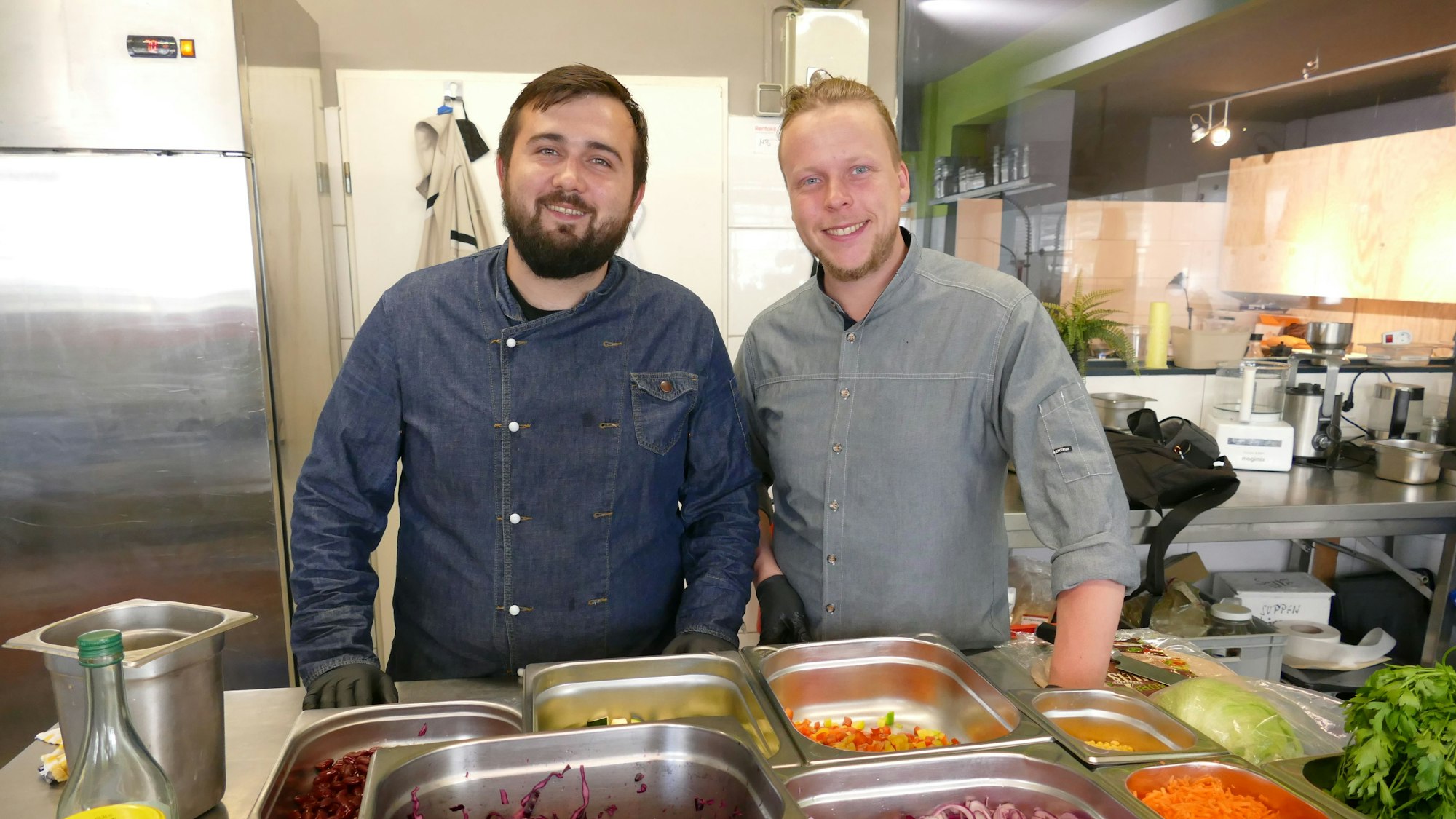 Zwei Männer in einer Küche vor frischen Zutaten