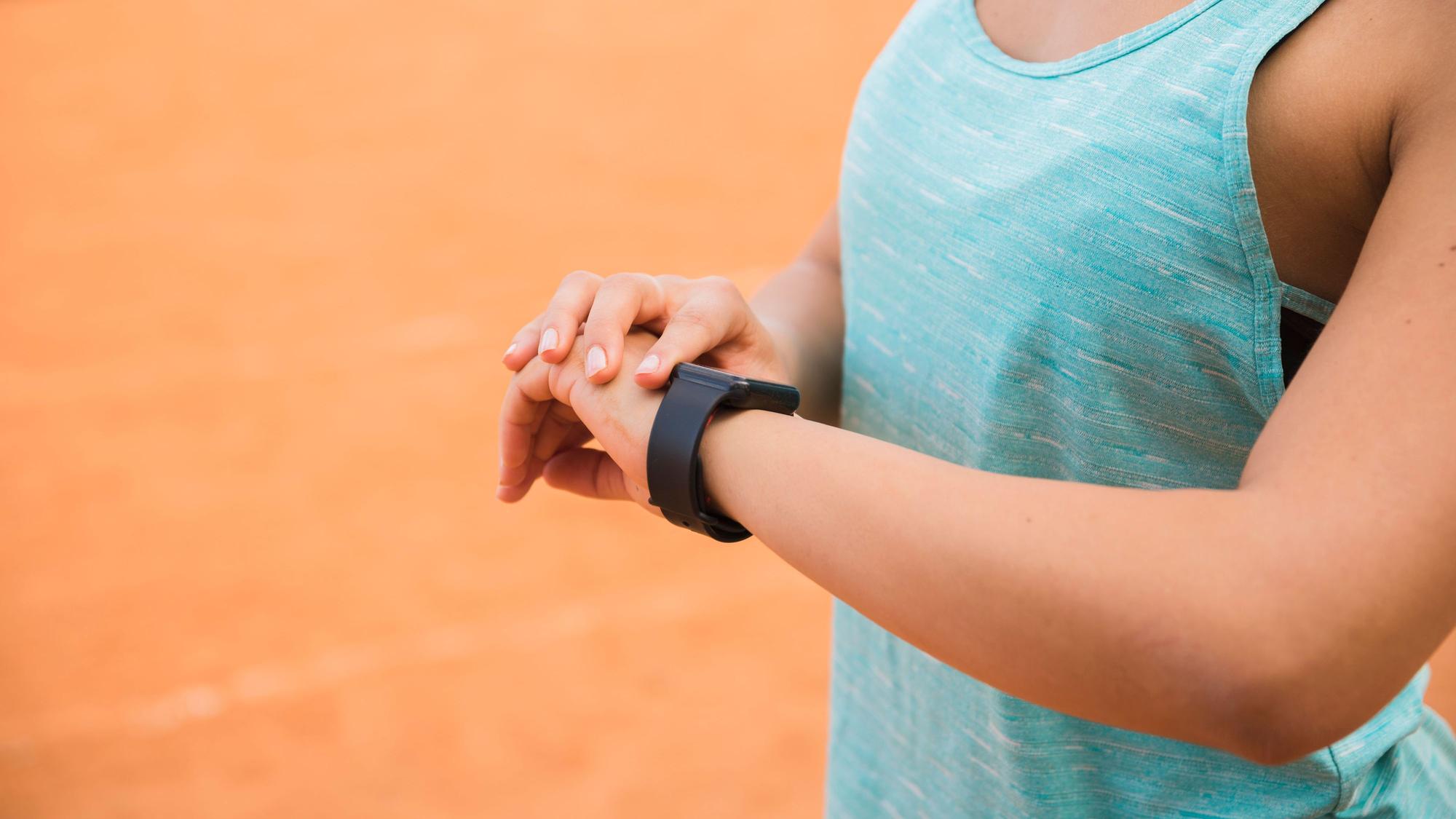 Eine Frau in Sportkleidung schaut auf ihre Fitnesstracker-Uhr.