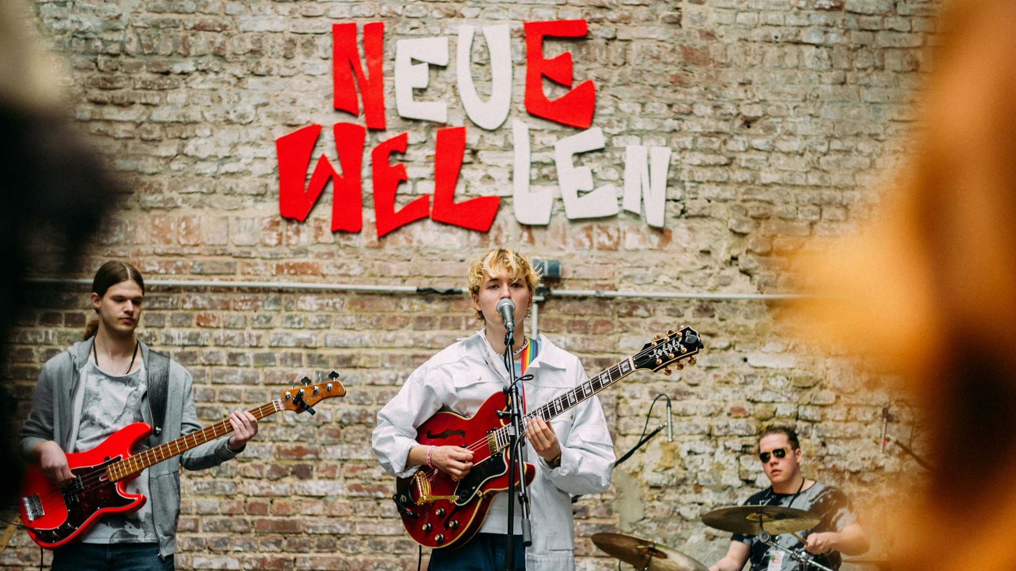 Ein Musiker steht auf einer Bühne. An der Wand steht in großen Lettern Neue Wellen.