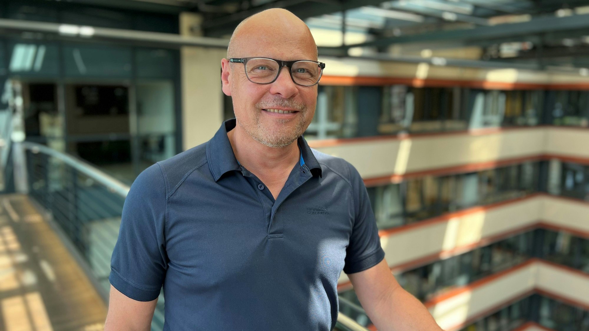 Ein Mann steht in einem Gebäude und lächelt in die Kamera.