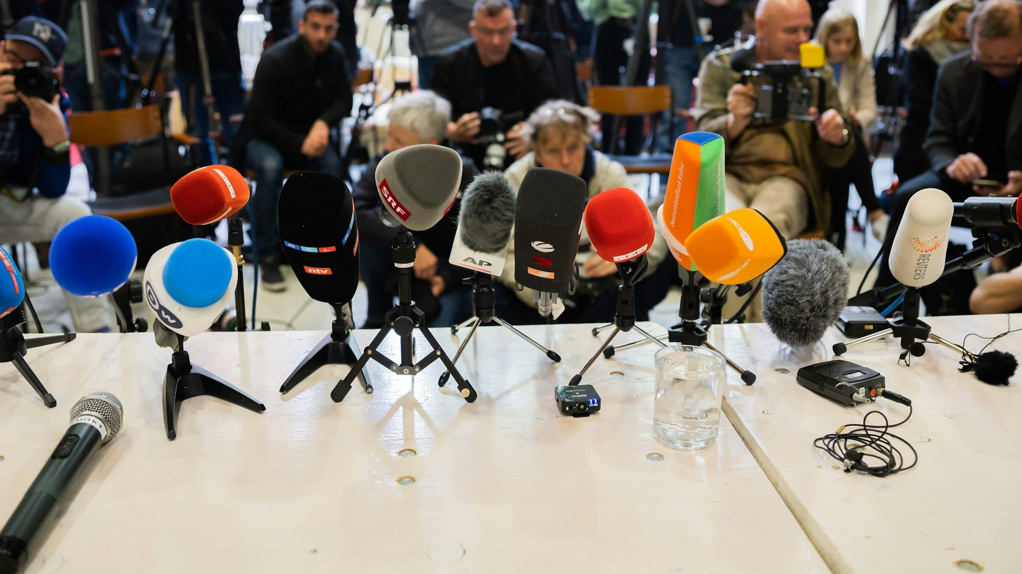 Ein Symbolbild zeigt zahlreiche Mikrofone vor Beginn einer Pressekonferenz.