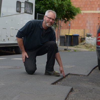 Ein Mann kniet an einer Fräskante in einer Straße, die eine Gefahrenquelle für Radfahrer sein kann.