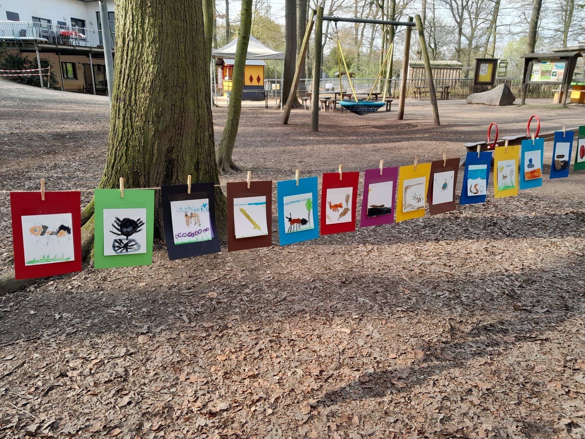 Gemalte Bilder zwischen Bäumen vor einem Spielplatz.