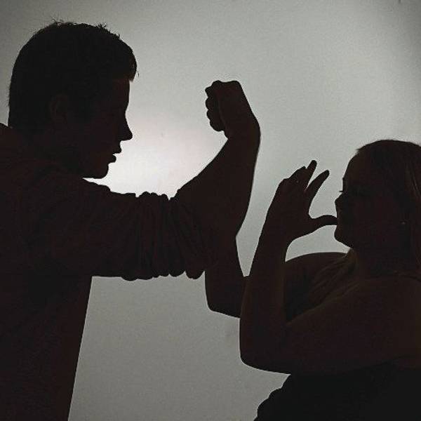 Ein als Silhouette abgebildeter Mann droht einer Frau mit der Faust.