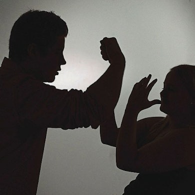 Ein als Silhouette abgebildeter Mann droht einer Frau mit der Faust.