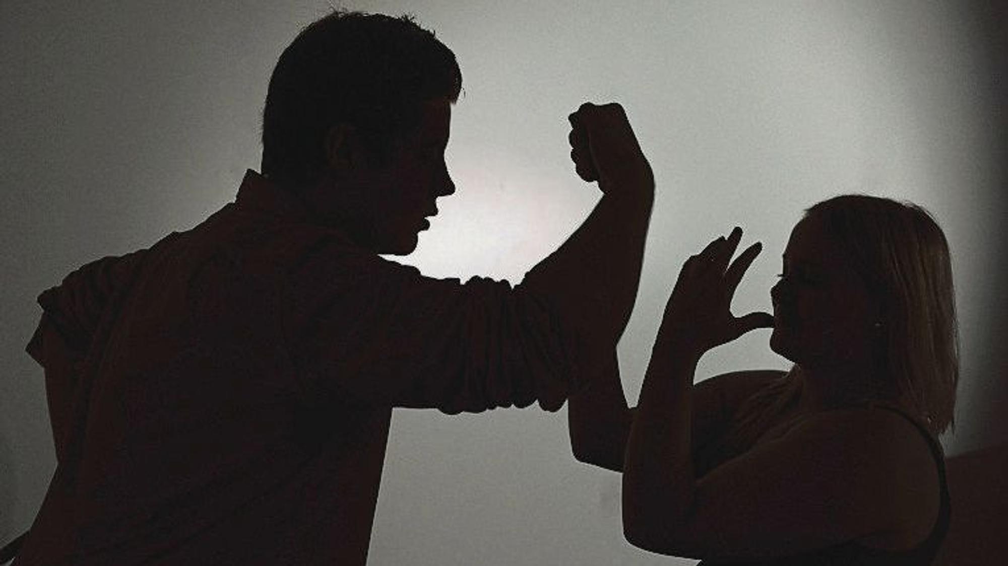 Ein als Silhouette abgebildeter Mann droht einer Frau mit der Faust.