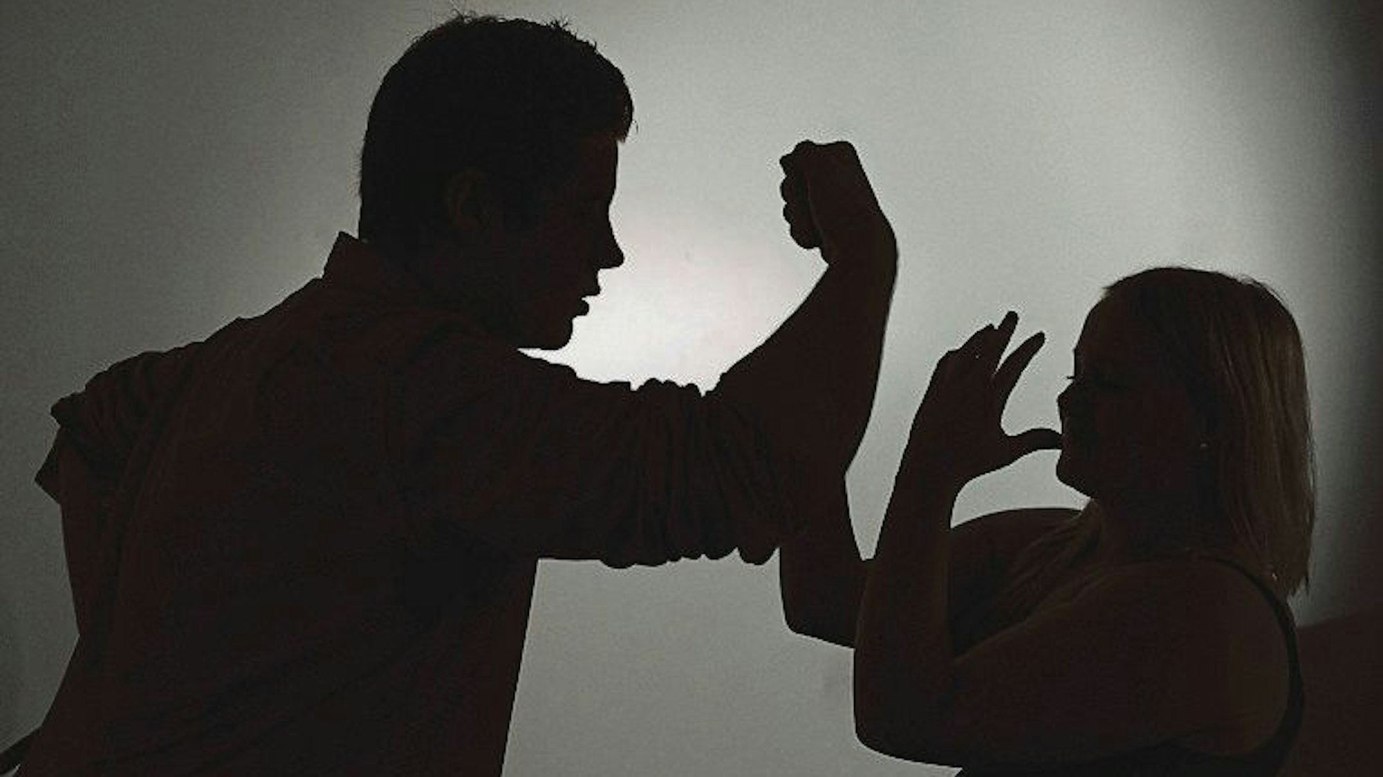 Ein als Silhouette abgebildeter Mann droht einer Frau mit der Faust.