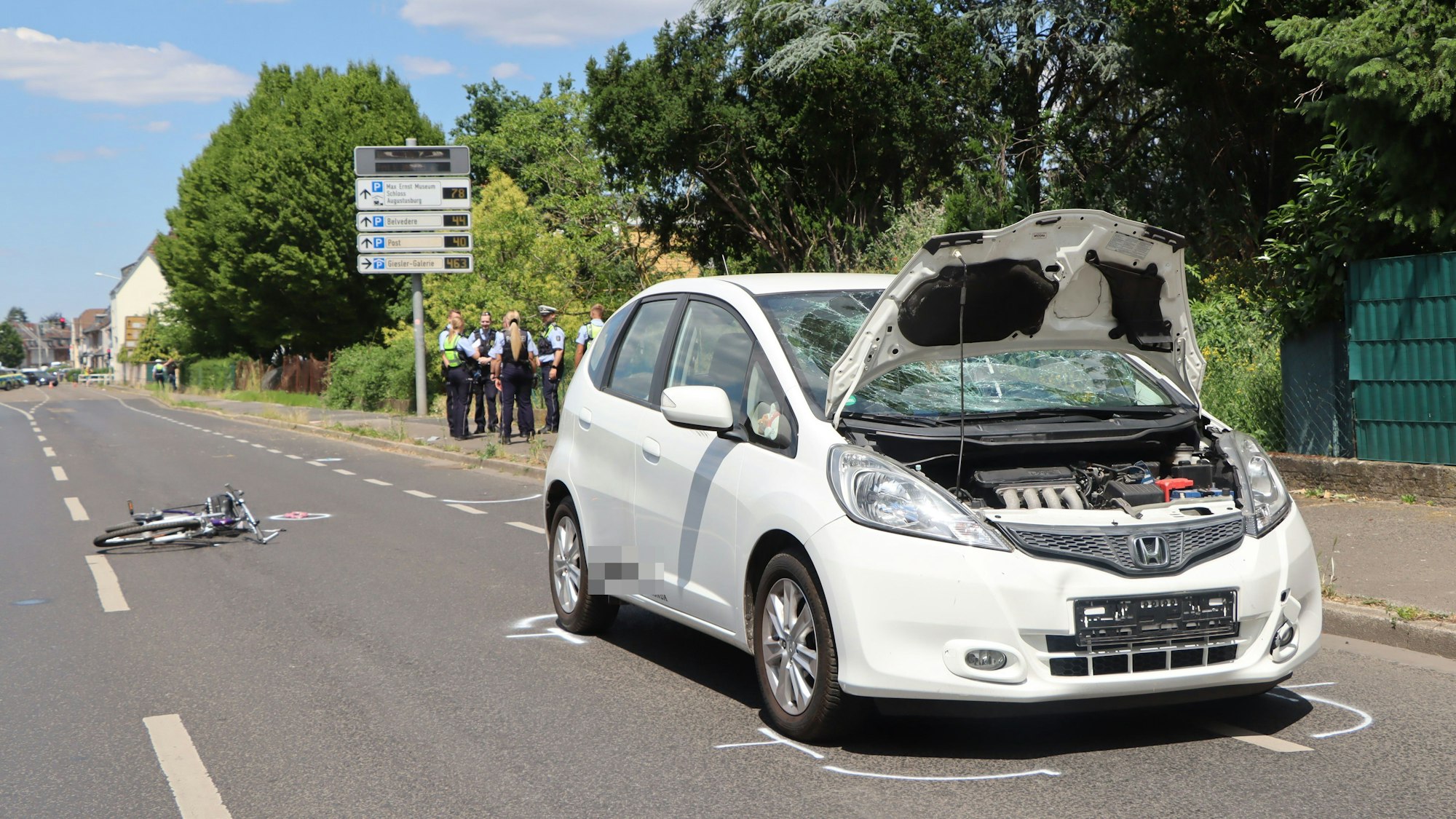 Ein Auto steh auf der Straße mit offener Motorhaube, dahinter liegt ein Fahrrad auf der Seite.