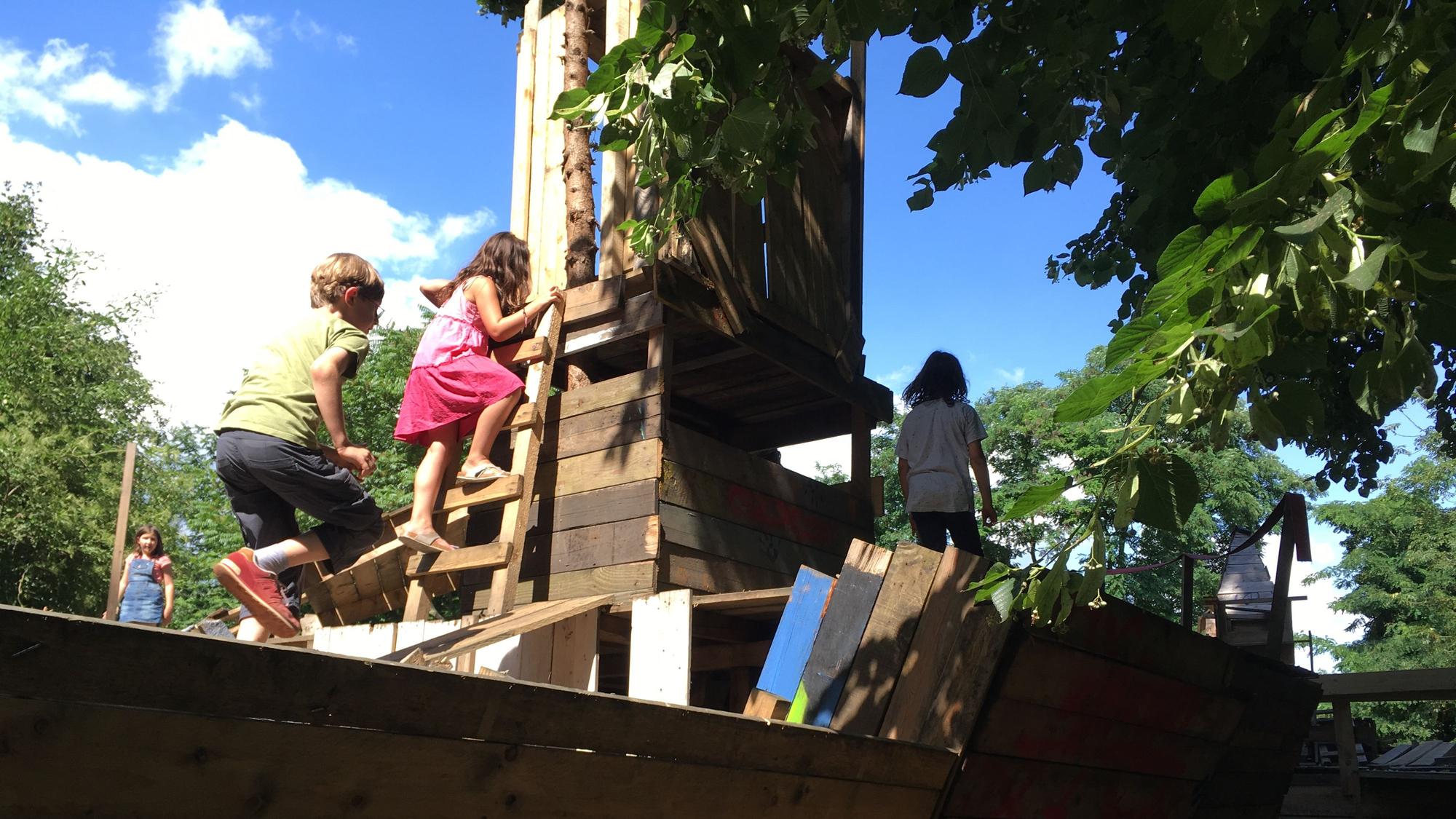 Kinder klettern auf einem Schiff aus Holz auf dem Bauspielplatz.