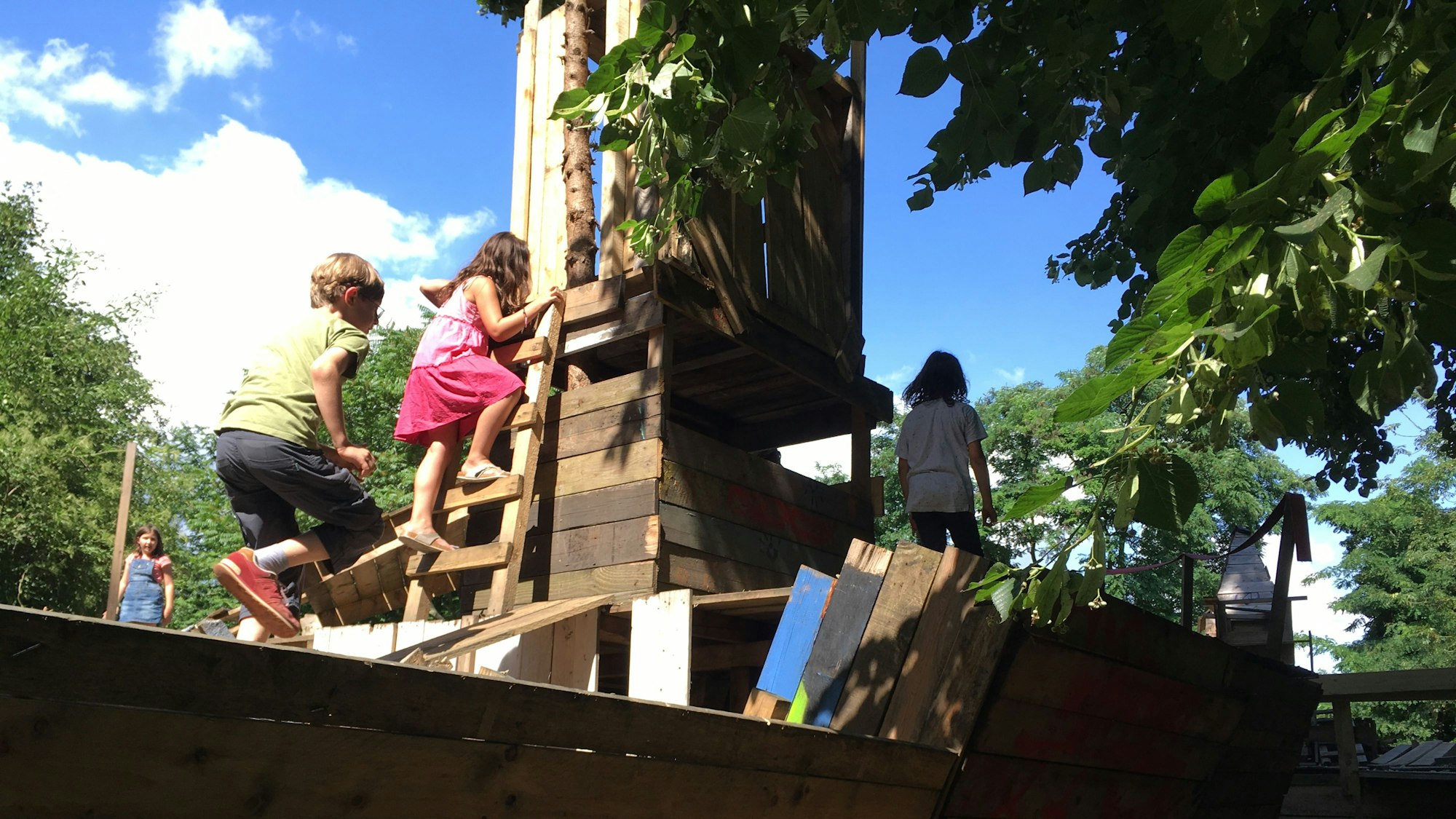 Kinder klettern auf einem Schiff aus Holz auf dem Bauspielplatz.