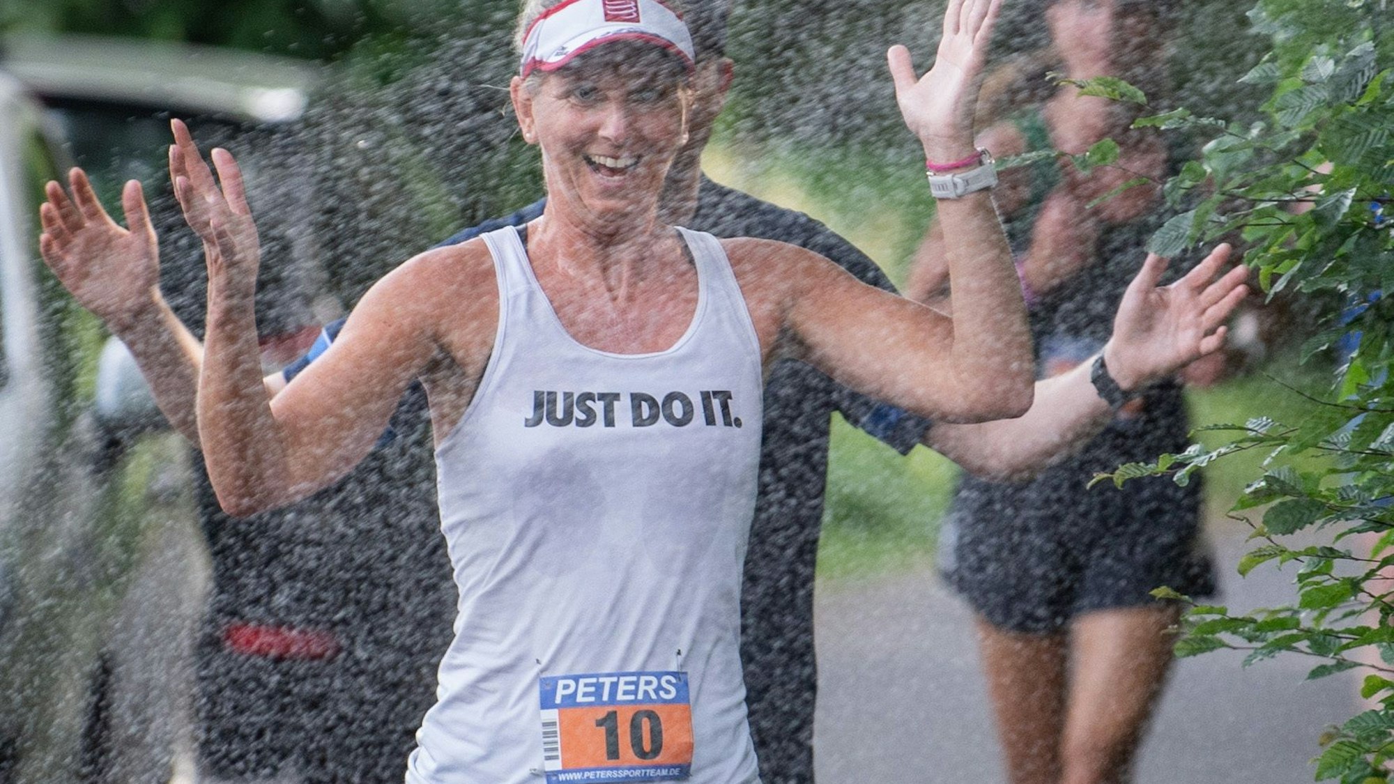 Eine Läuferin freut sich über das Wasser, das aus einer Dusche ins Läuferfeld gespritzt wird.