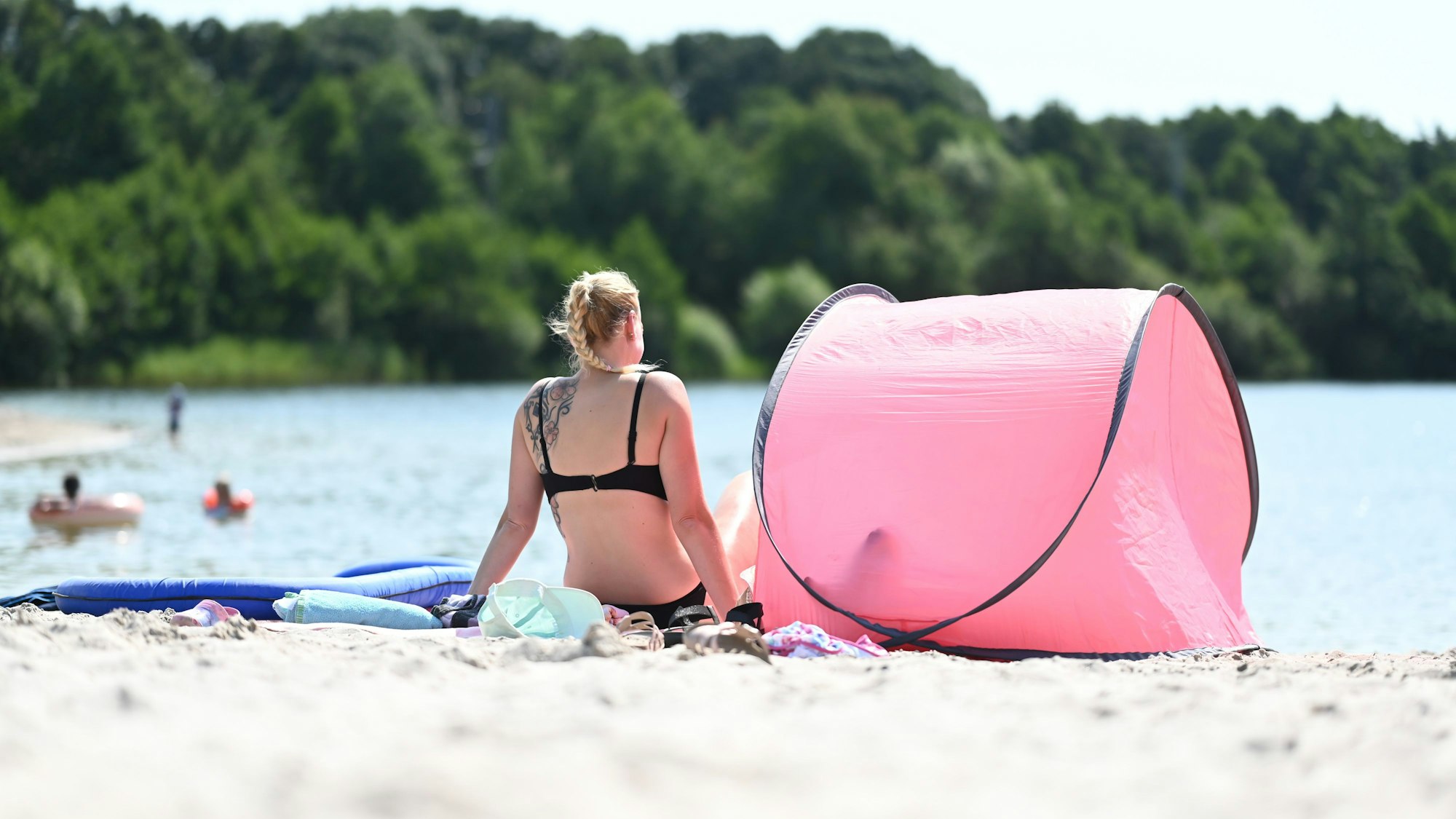 Eine Frau sitzt im Strand an einem Badesee (Archivfoto).