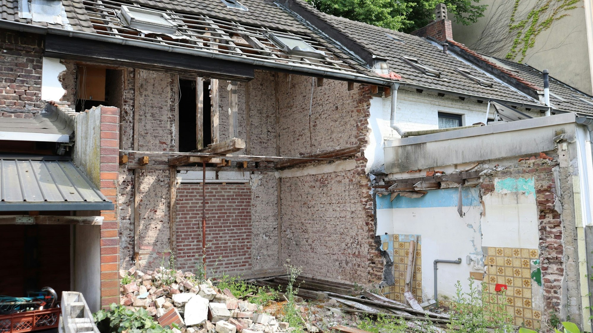 Ein zur Hälfte abgerissenes Reihenhaus ist zu sehen. Im Garten liegen Mauerreste.