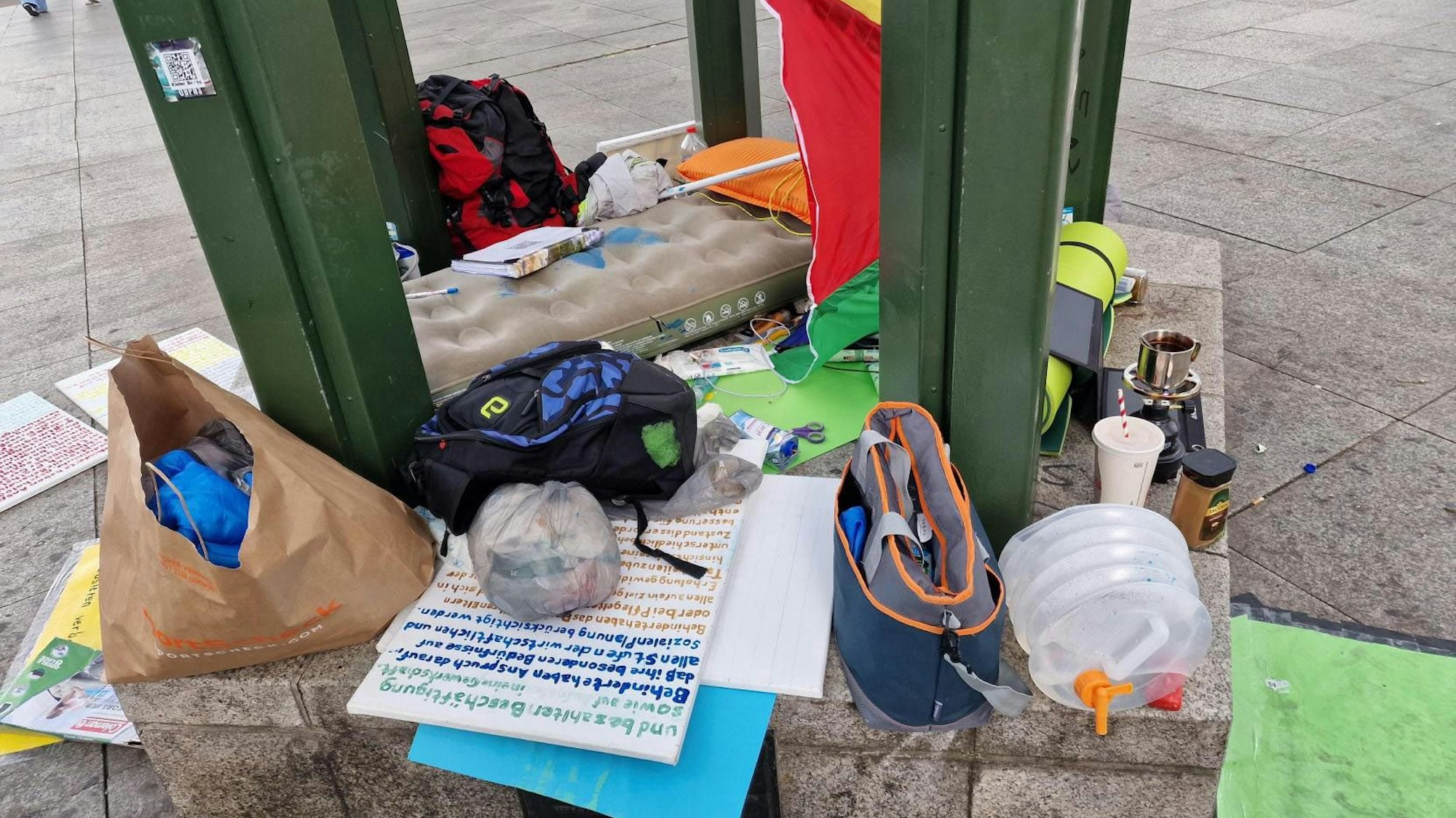 Bunte Plakate, ein Regenschirm und eine Luftmatratze schmücken den derzeitigen Schlafplatz von Ilias Emmanuil.