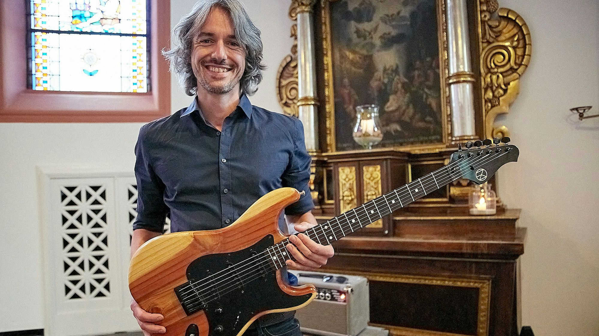 Ein Mann hält eine Gitarre in den Händen, die er aus dem Holz eines bei der Flutkatastrophe zerstörten Baums gebaut hat.