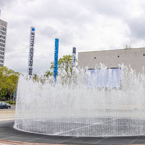 Ein Springbrunnen spritzt Wasser vor der Bundeskunsthalle. Am Rand stehen 16 Säulen, die die Bundesländer symbolisieren.