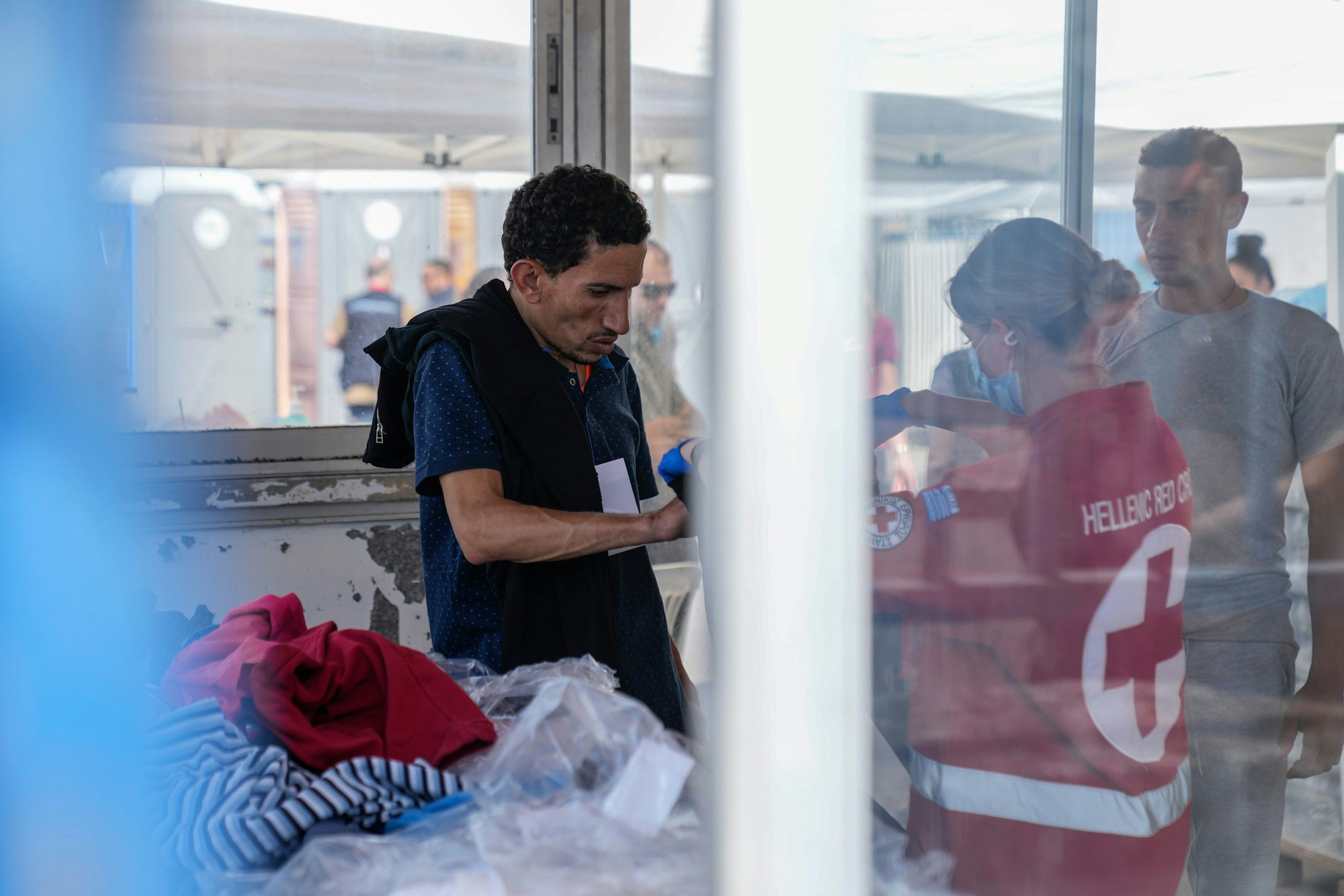 Eine Freiwillige des griechischen Roten Kreuzes gibt einem Überlebenden eines Bootsunglücks Kleidung vor einem Lagerhaus. Die 104 überlebenden Migranten eines Bootsunglücks vor Griechenland sollen am Donnerstag und Freitag in ein Flüchtlingslager nahe Athen gebracht werden. Zudem ist die Überführung der Toten nach Athen angelaufen, wie der Staatssender ERT berichtete. Dort sollen DNA-Proben genommen werden, um die Menschen zu identifizieren.