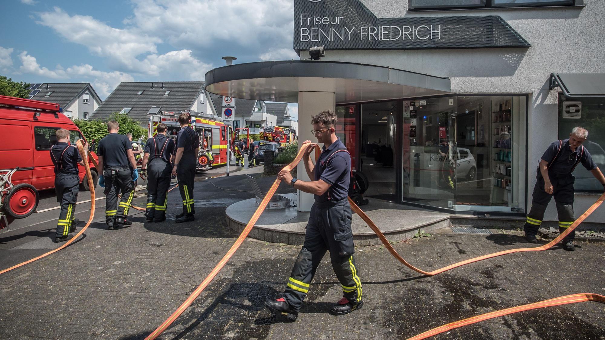 Feuerwehrleute verlegen vor einem Friseursalon Schläuche.