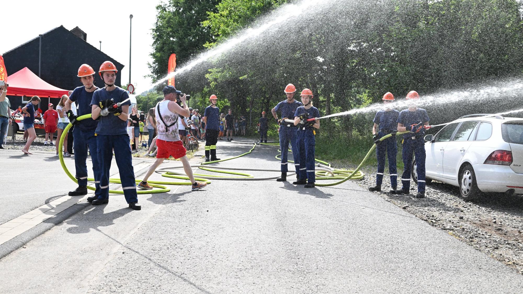 Mehrere junge Feuerwehrleute schießen Wasser aus zwei Schläuchen.