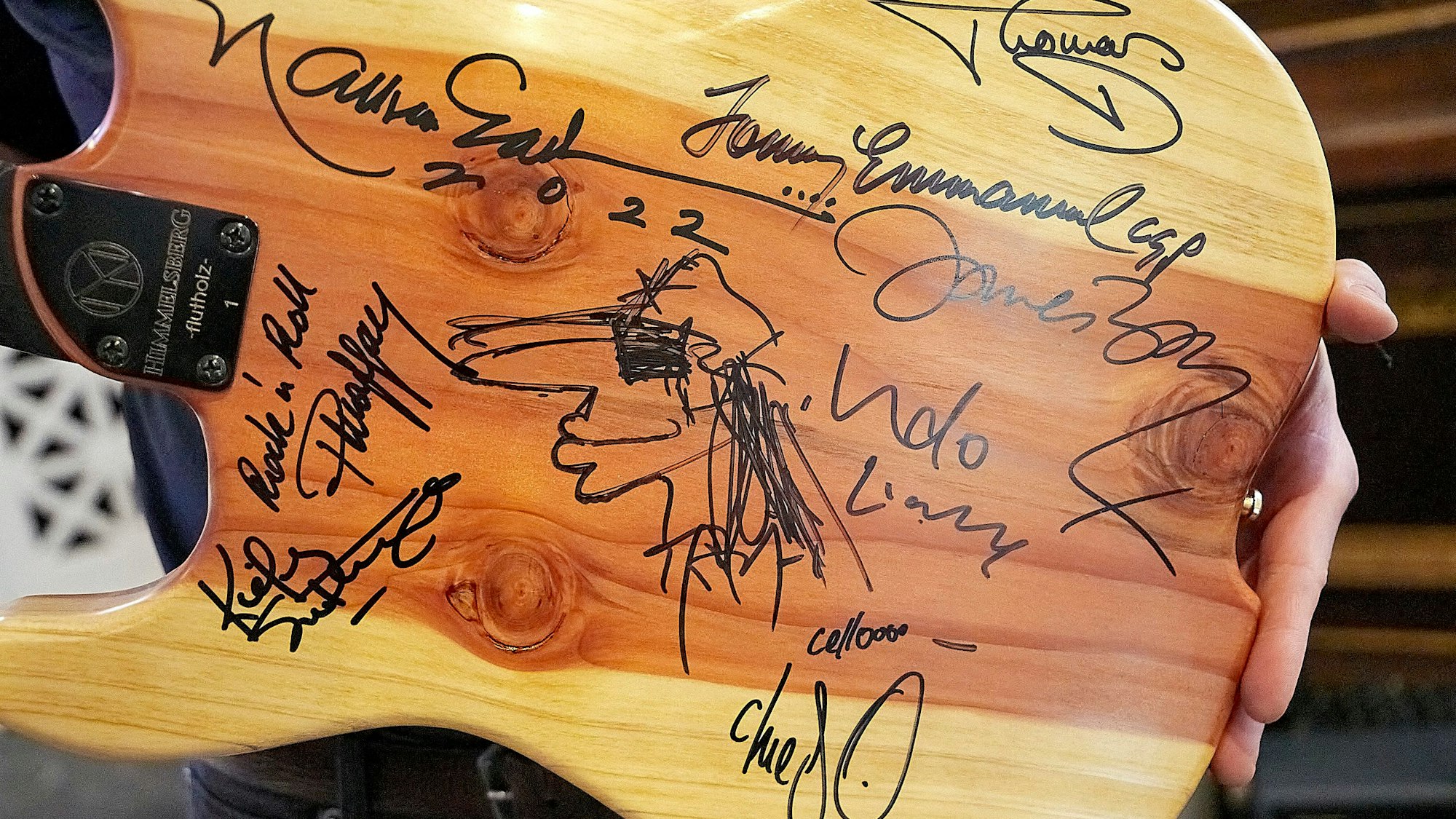 Auf der Rückseite einer Gitarre sind zahlreiche Unterschriften von bekannten Musikern zu sehen.