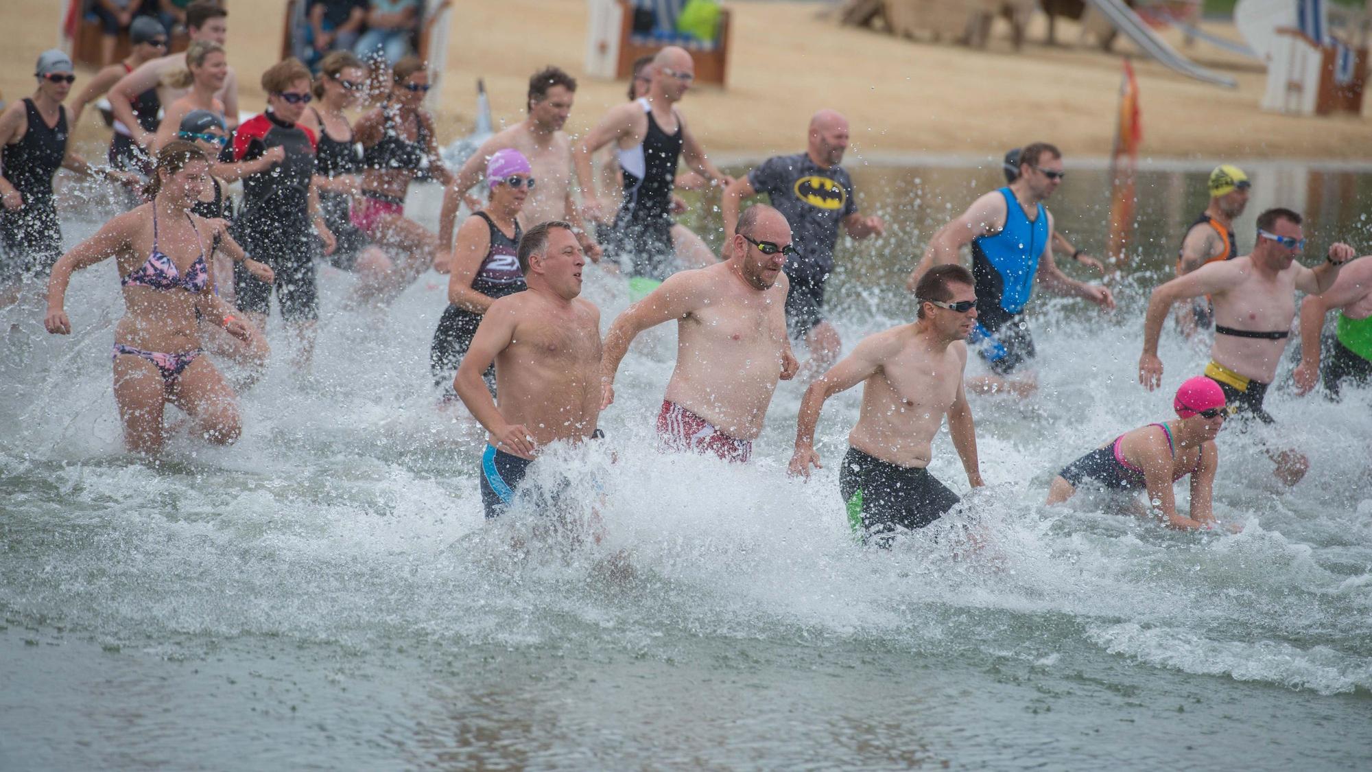 Menschen in Badekleidung laufen für einen Triathlon in den Zülpicher Wassersportsee.