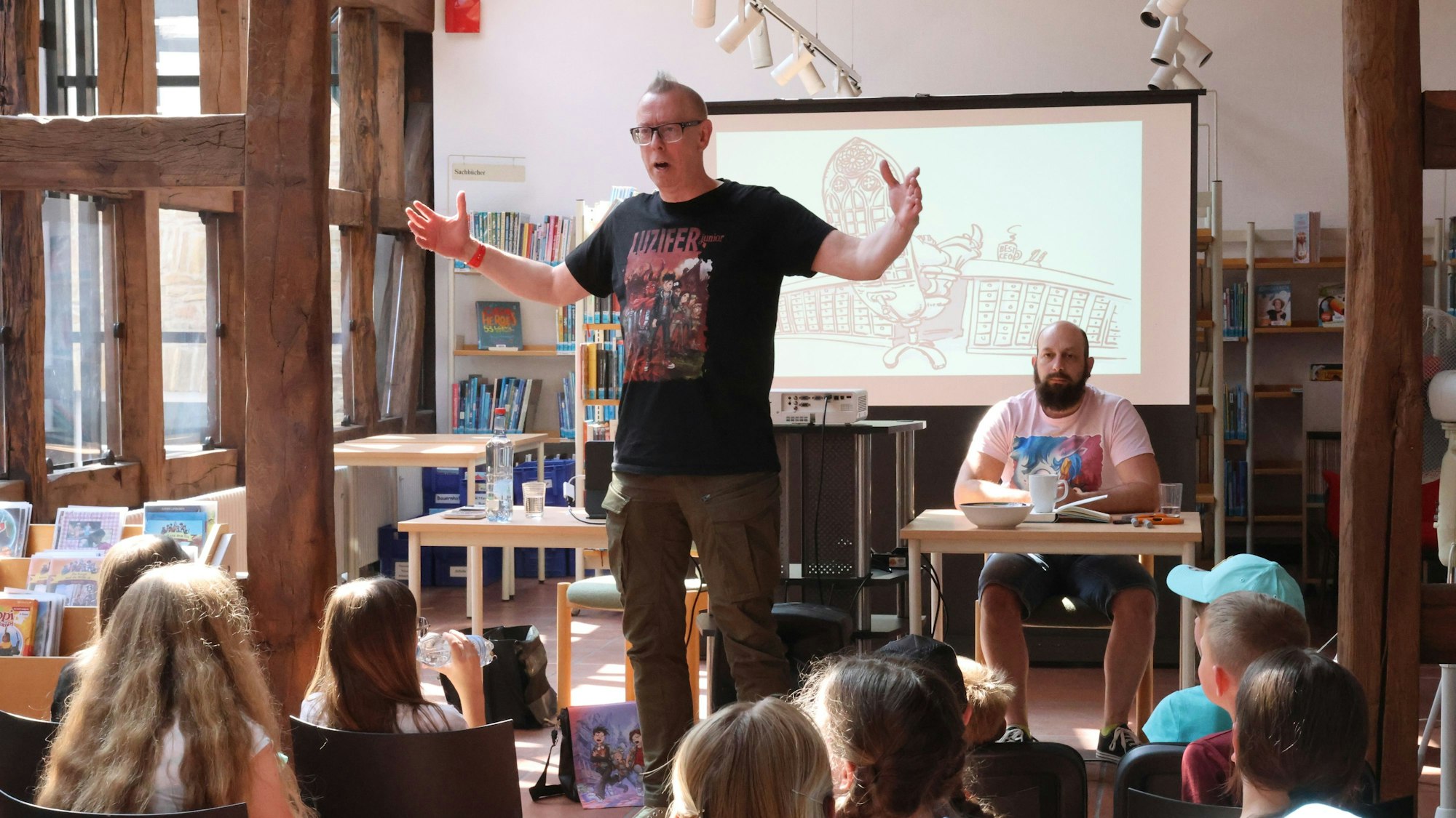 Der Autor Jochen Till und der Zeichner Raimund Frey treten vor einer Leinwand in der Bücherei auf.