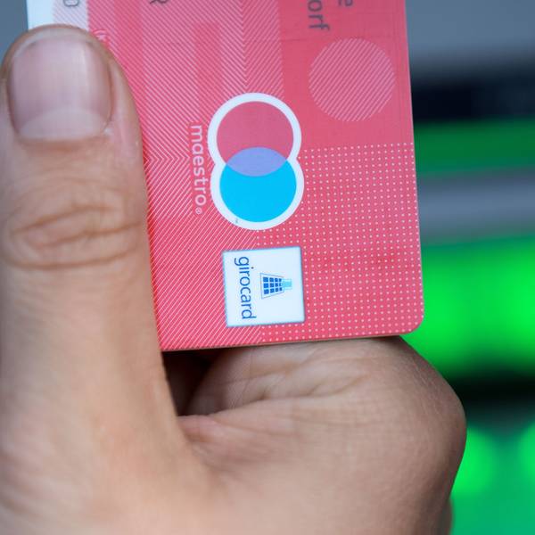 Eine Person hält vor einem Geldautomaten eine Girocard in der Hand. Auf der Karte ist das Maestro-Logo zu sehen.